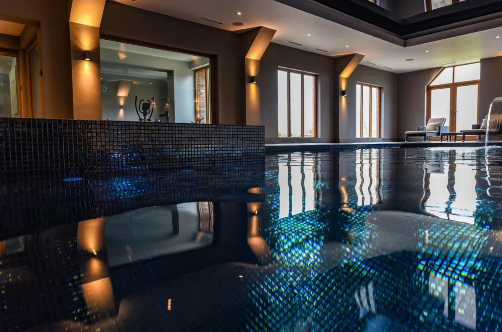 Luxury indoor swimming pool with dark mosaic tiles and warm lighting