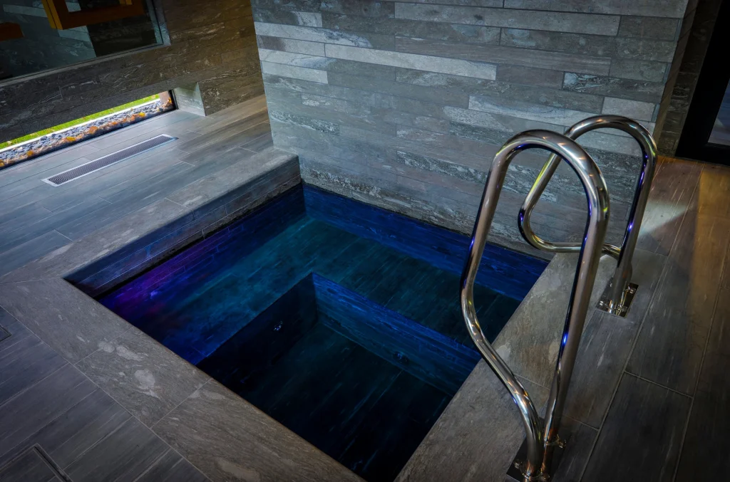 Modern indoor plunge pool with blue lighting and steel handrails