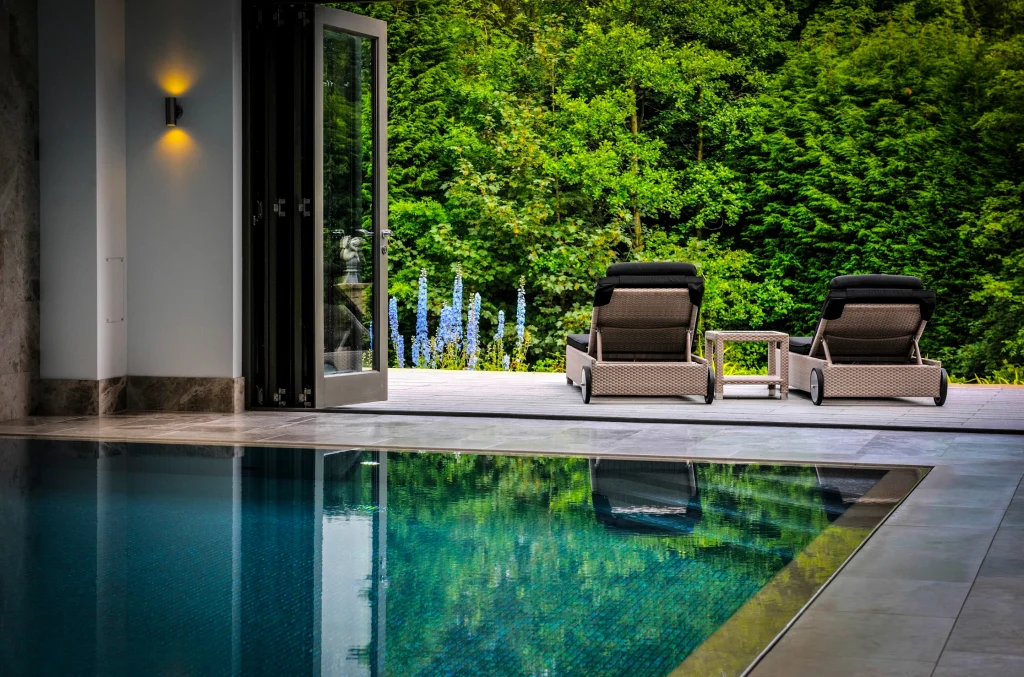 Modern poolside terrace with lounge chairs and lush green backdrop