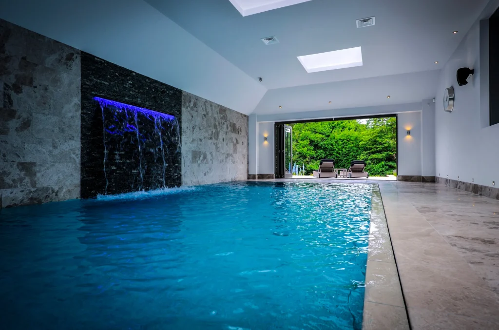 Modern indoor swimming pool with waterfall feature and garden view