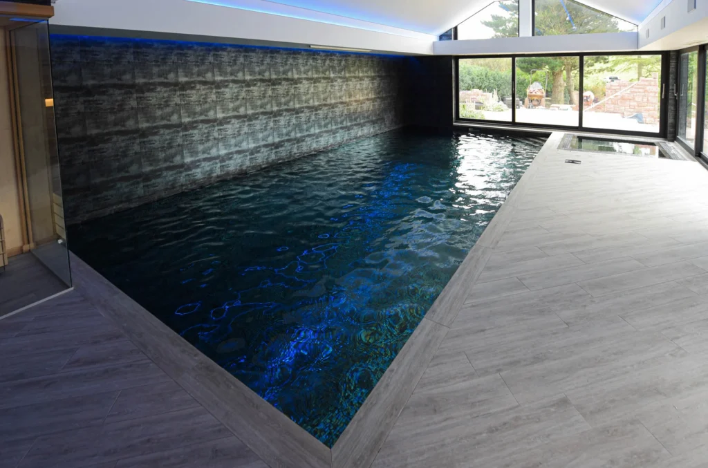 Modern indoor swimming pool with blue lighting and large windows