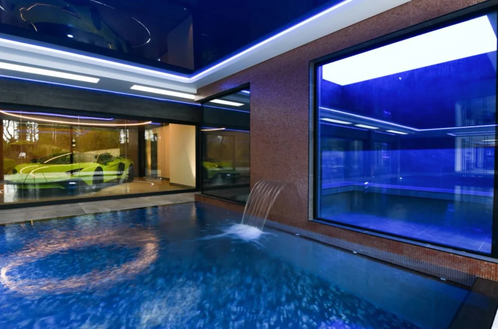 Modern indoor swimming pool with blue neon lighting and waterfall feature