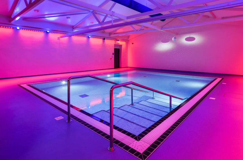 Modern indoor swimming pool with vibrant neon pink and blue lighting